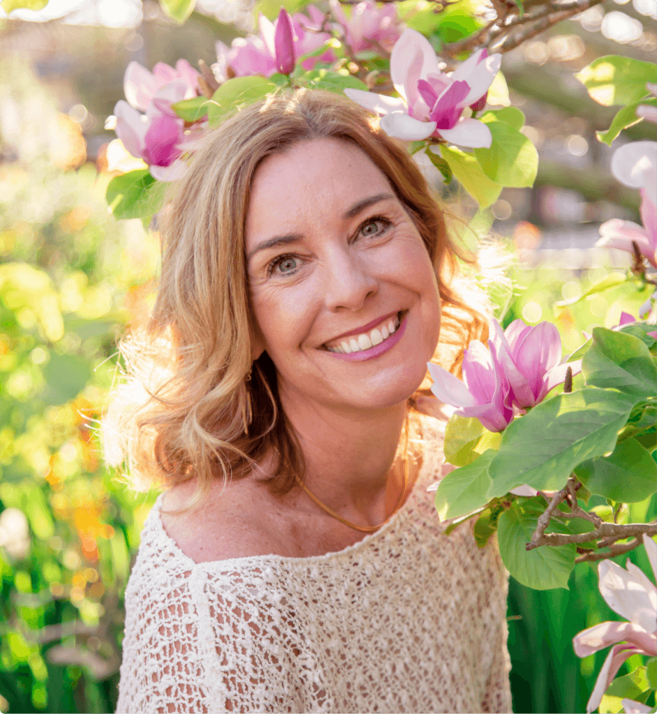 Shawna Robins is standing next to a tree with purple flowers. She is wearing a white top and smiling at the camera.